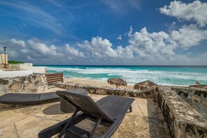 A beachside patio with lounge chairs, a stone wall, and a view of the ocean. - Luxury Ocean View Villa - Hotel Zone Solymar Condo Villa 11 (Cancún)