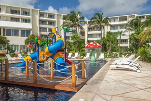A water park with slides and a mushroom fountain, surrounded by palm trees and a pool with lounge chairs. - Luxury Ocean View Villa - Hotel Zone Solymar Condo Villa 11 (Cancún)