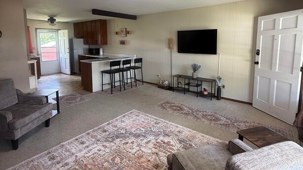 A living room with a large rug, two sofas, a TV, and a kitchen in the background.