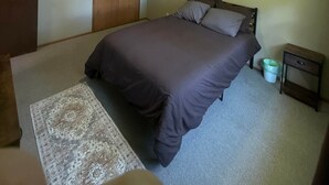 A bedroom with a bed, a nightstand, a waste bin, a door, and a ceiling light.