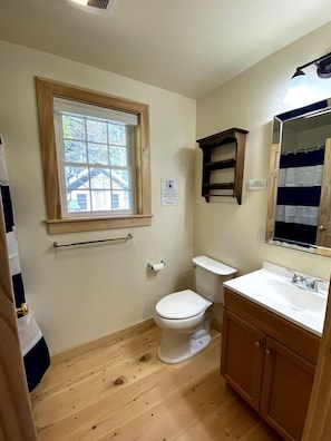 Ein kleines Badezimmer mit Fenster, Toilette, Waschbecken und Spiegel.