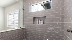 Une salle de bain moderne avec des carreaux gris, une fenêtre et une étagère où sont rangés les produits de toilette.