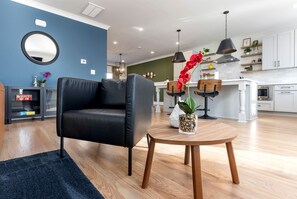 Ein modernes Wohnzimmer mit einem schwarzen Ledersofa, einem runden Couchtisch mit einer Pflanze und einer Küche im Hintergrund.
