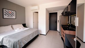 A modern hotel room with a bed, a kitchenette, and a door leading to another room. - Vnc consolation apt 614 (São Paulo)