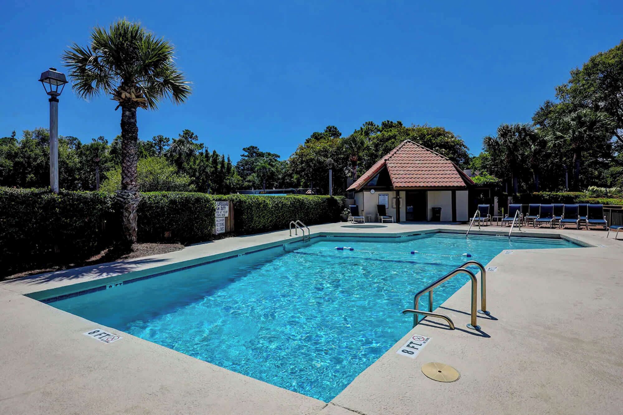 A swimming pool with a lifeguard station, lounge chairs, and a small building with a red roof.