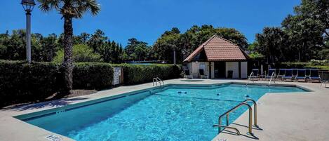 A swimming pool with a lifeguard station, lounge chairs, and a small building with a red roof.