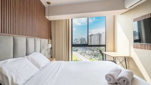 Habitación de hotel con una cama grande, vistas a la ciudad y un televisor montado en la pared.