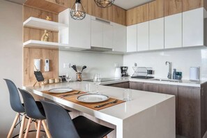 Eine moderne Küche mit weißen Schränken, einer zentralen Kochinsel mit Sitzgelegenheit und einer Wand in Holzoptik.