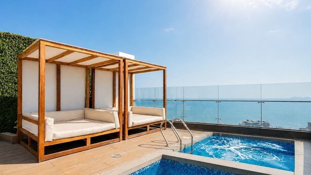 Zona de piscina en la azotea con una pérgola de madera y sillones de descanso, con vista a un mar azul y despejado.