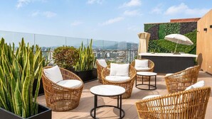 Una terraza en la azotea con muebles de mimbre, una zona de bar y vistas a la ciudad.