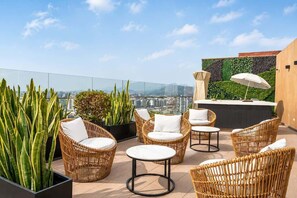 Eine Dachterrasse mit Korbmöbeln, einer Bar und Blick auf die Stadtlandschaft.