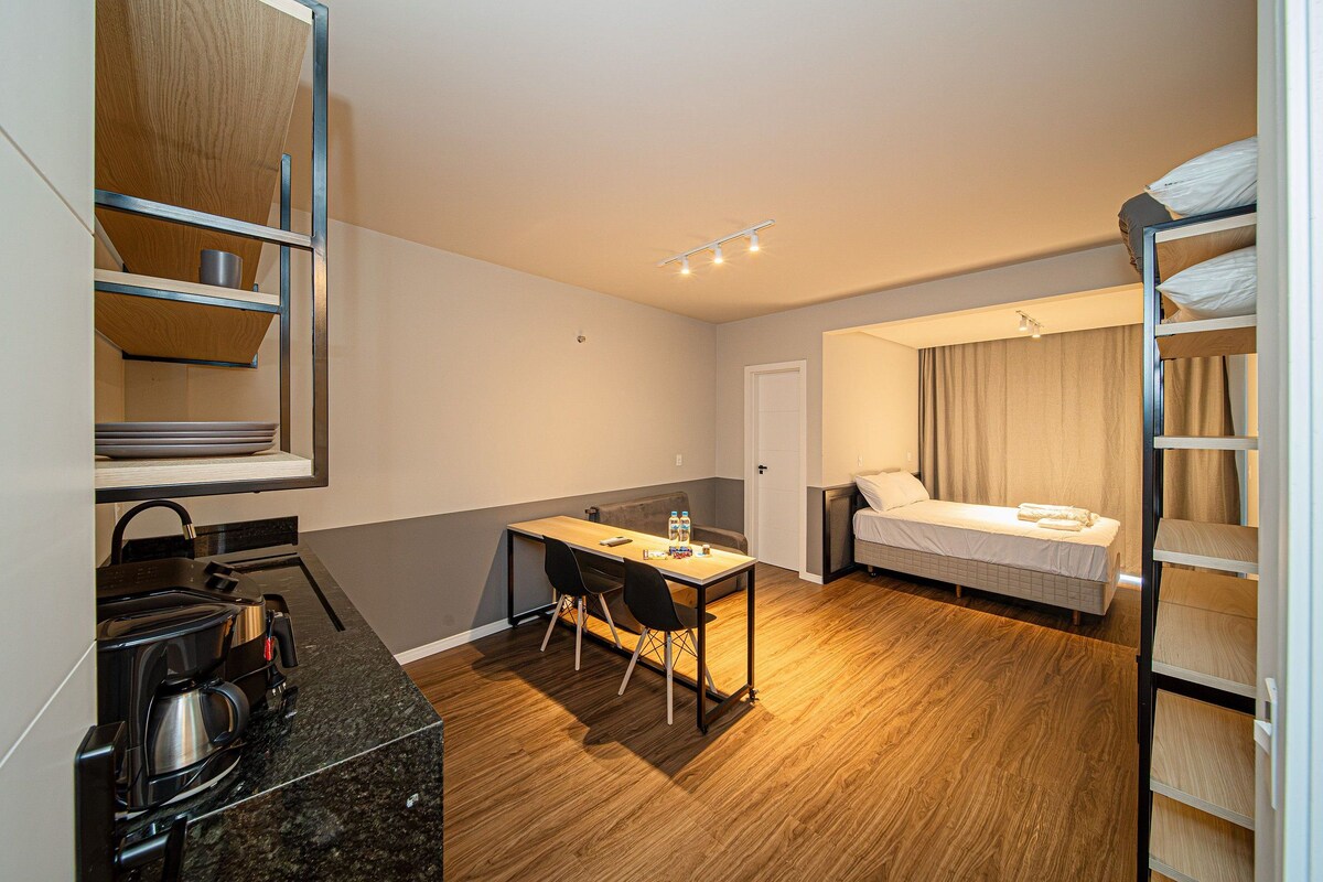 A compact hotel room with a kitchenette, a single bed, and a small desk area.