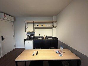 Une petite cuisine équipée d’une machine à café, d’un évier et d’un four à micro-ondes. On y trouve une table avec une télécommande et un magazine.
