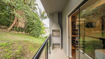 Un balcón con vista a un jardín exuberante y una parrilla moderna al aire libre.