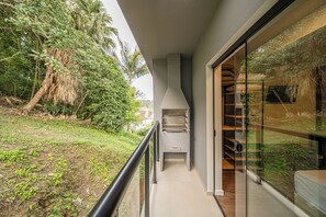 A balcony with a view of a lush garden and a modern outdoor grill. - Apez Smart Studio (Joinville)