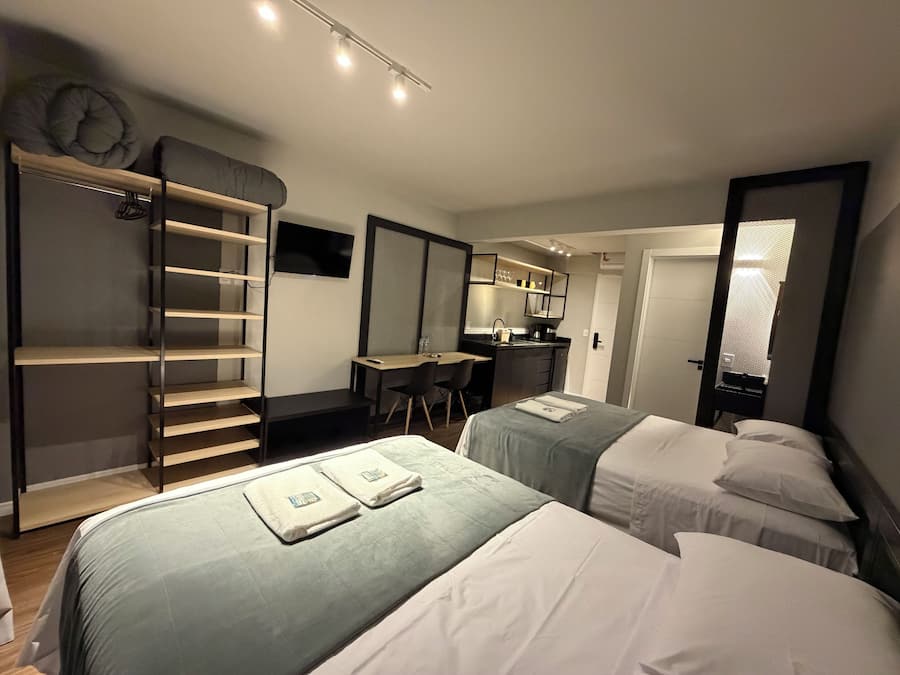 A hotel room with two beds, a desk, a wardrobe, and a kitchenette.