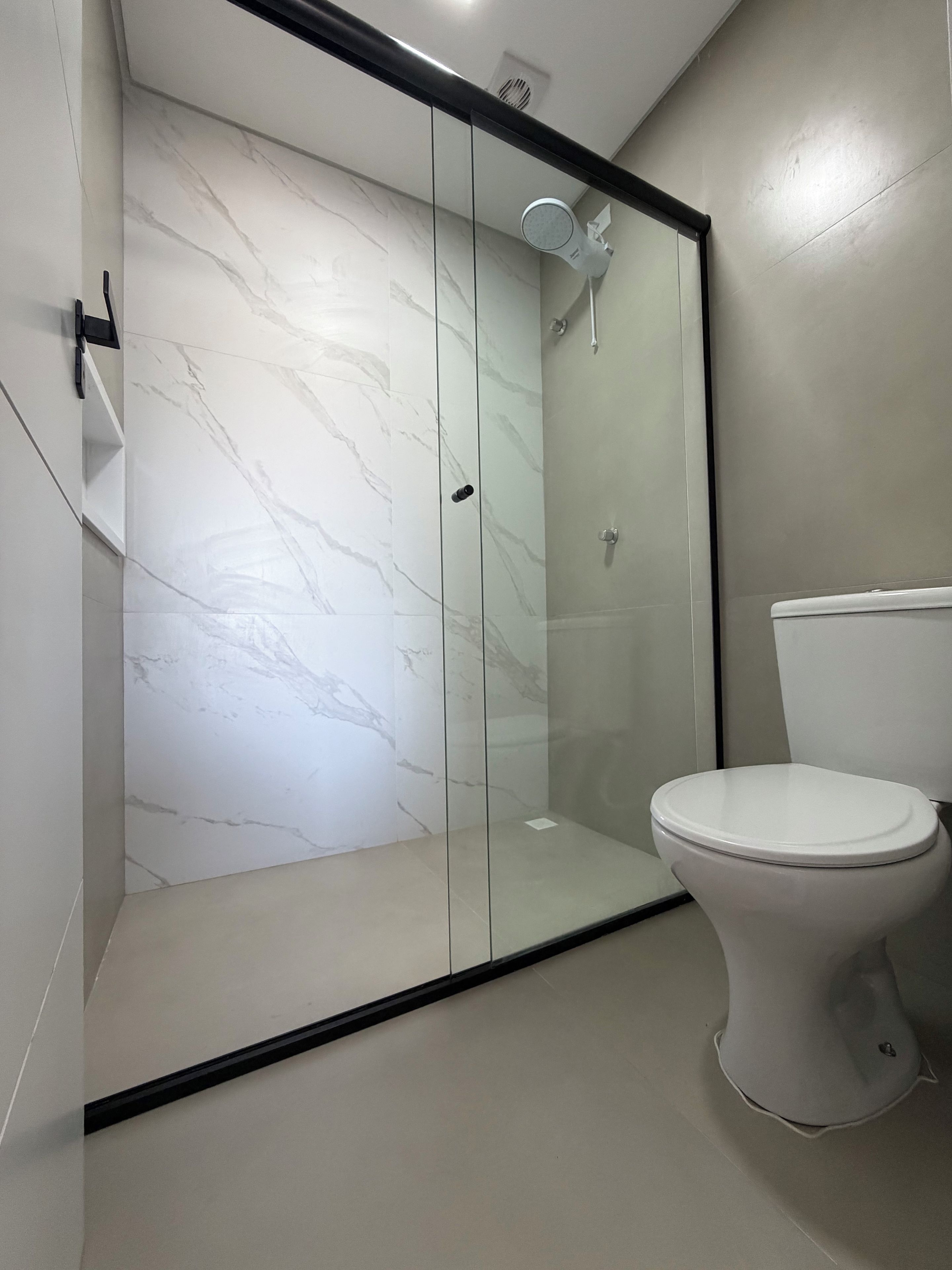 Un baño con ducha de vidrio, inodoro blanco y paredes con diseño de mármol.