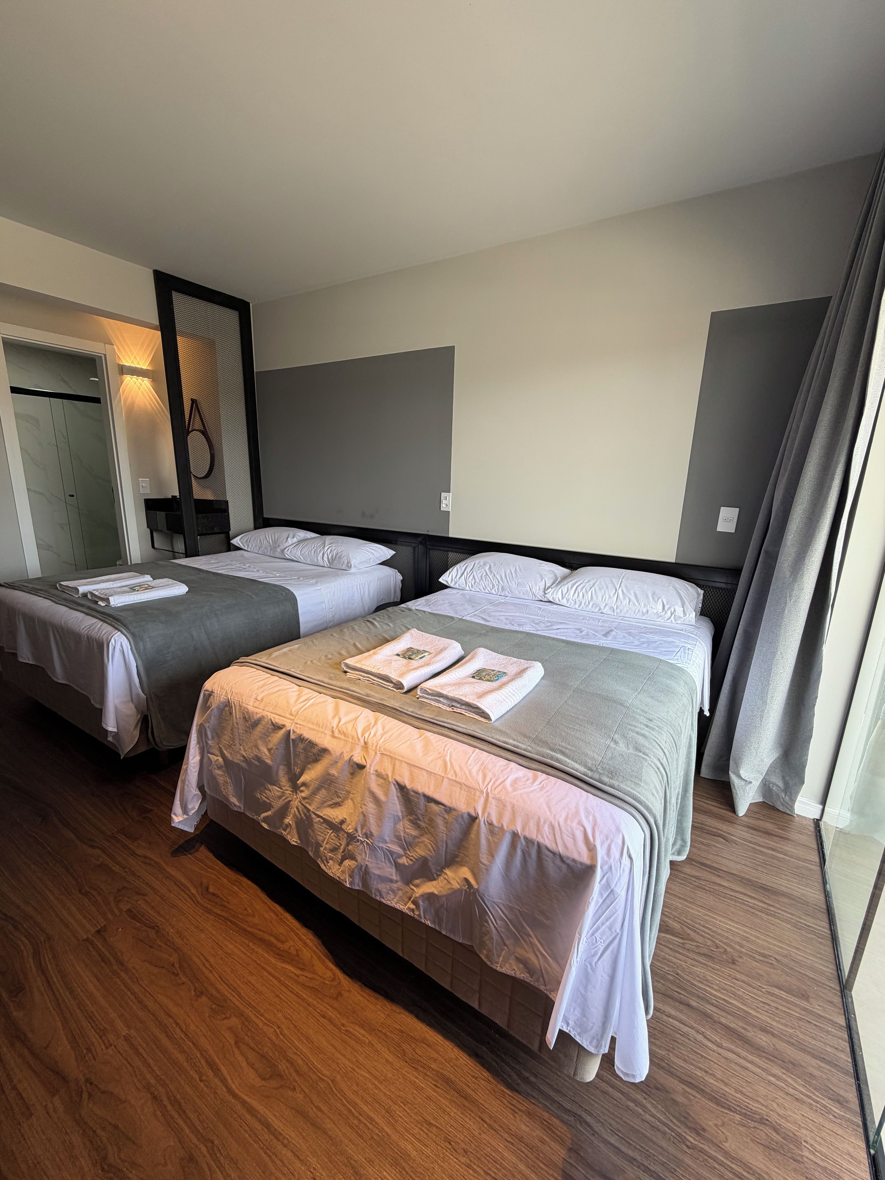 Ein Hotelzimmer mit zwei Betten, Holzboden und einem großen Fenster mit Vorhängen.