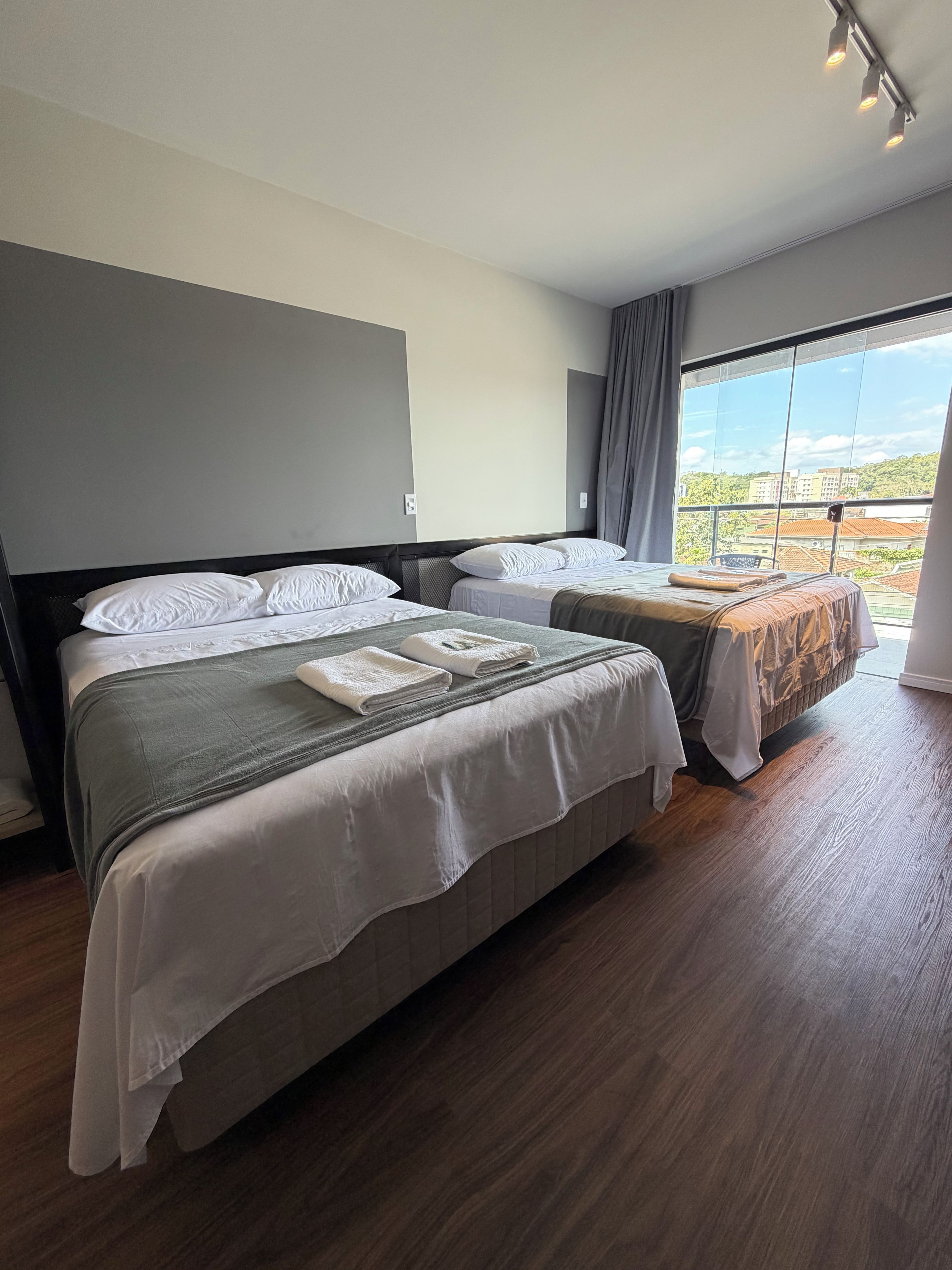 A hotel room with two beds, a large window, and a view of buildings.