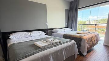 A hotel room with two beds, a large window, and a view of buildings.