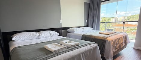 Habitación de hotel con dos camas, un ventanal grande y vistas a edificios.
