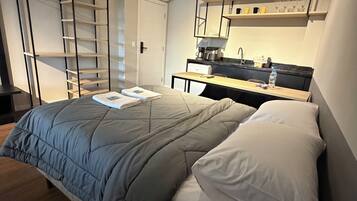 Un dormitorio con cama, escritorio, silla, armario y baño.