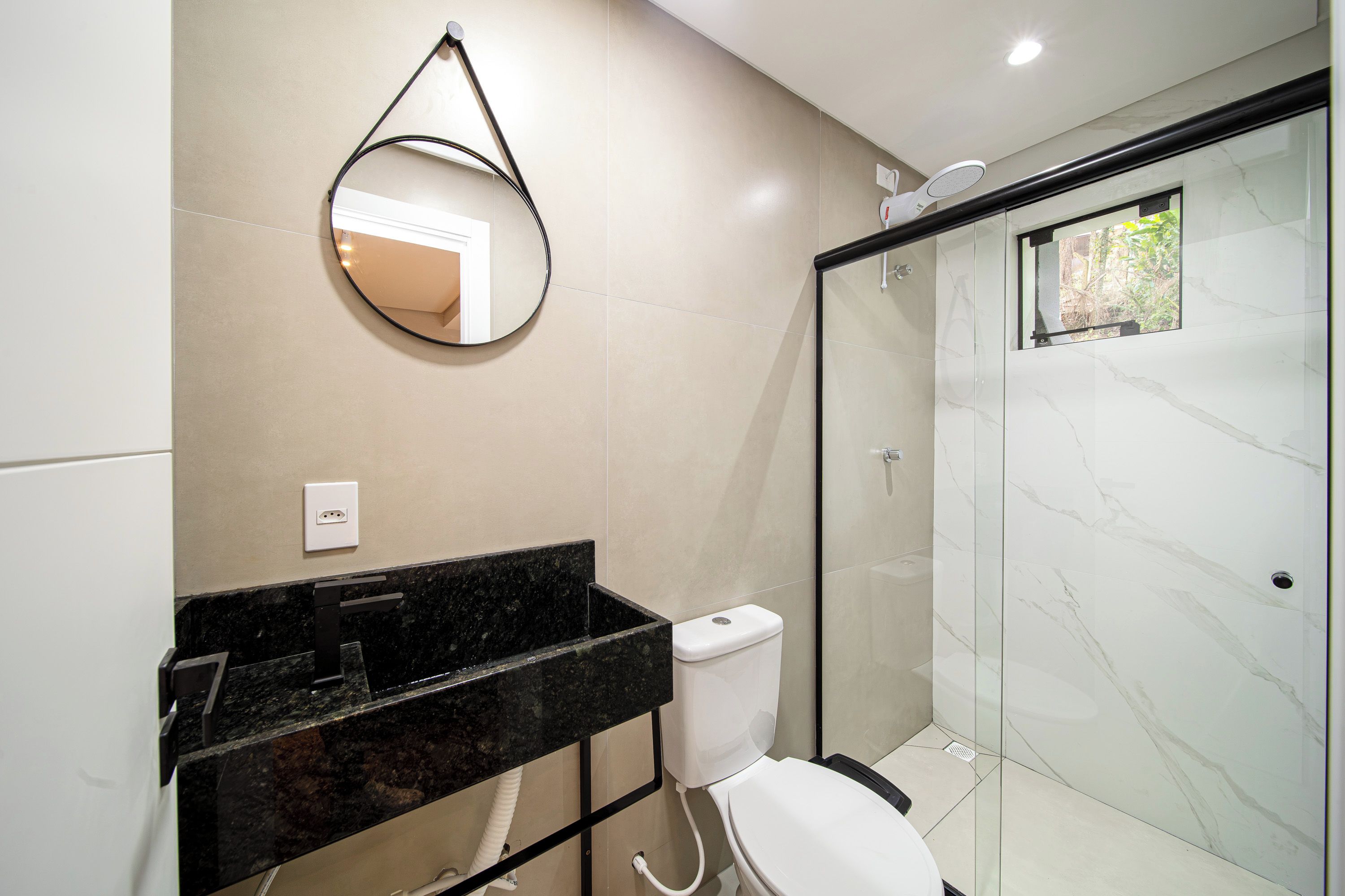 A modern bathroom with a glass shower enclosure, a black marble countertop, and a white toilet.