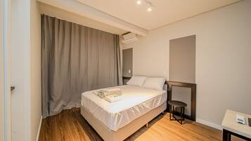 Ein Hotelzimmer mit einem Einzelbett, einem Nachttisch, einem Sessel und einem großen Fenster mit Vorhängen.