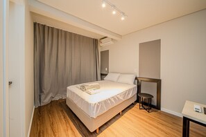 Une chambre d’hôtel avec un lit simple, une table de chevet, une chaise et une grande fenêtre avec des rideaux.