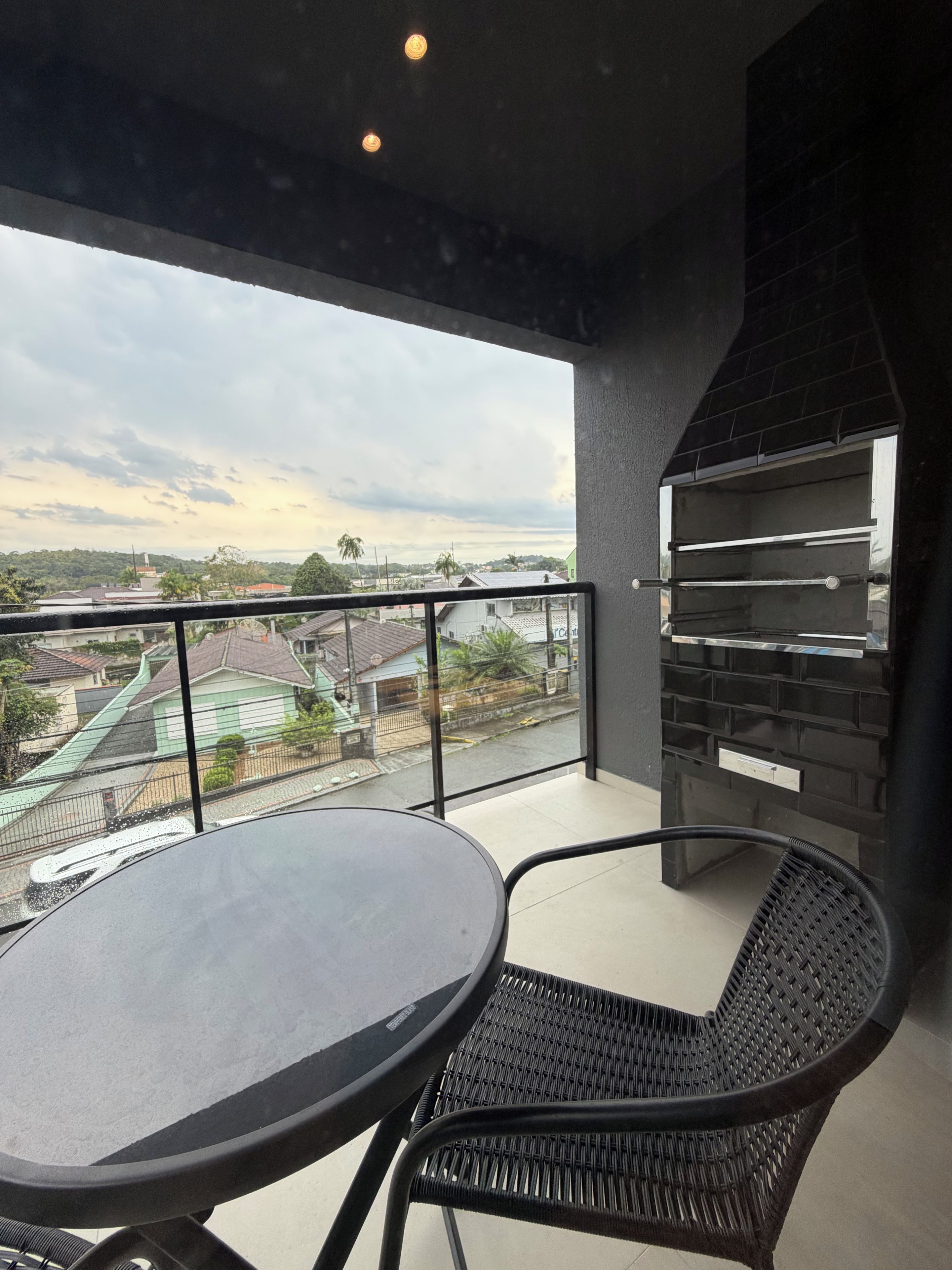 Un balcón con una mesa redonda y dos sillas, una parrilla y vistas a una zona residencial.