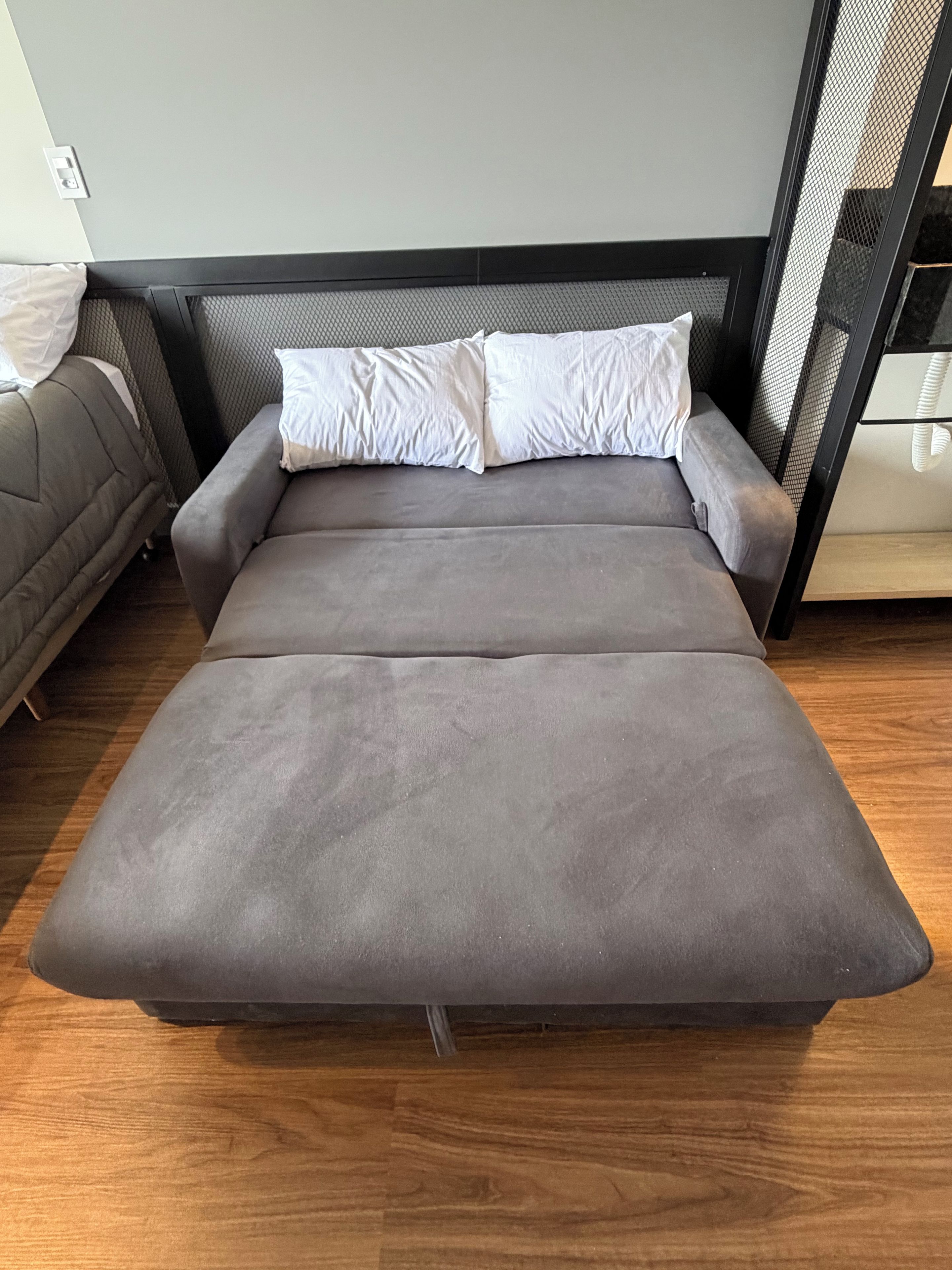 A modern bed with a grey mattress and white pillows in a room with wooden flooring.