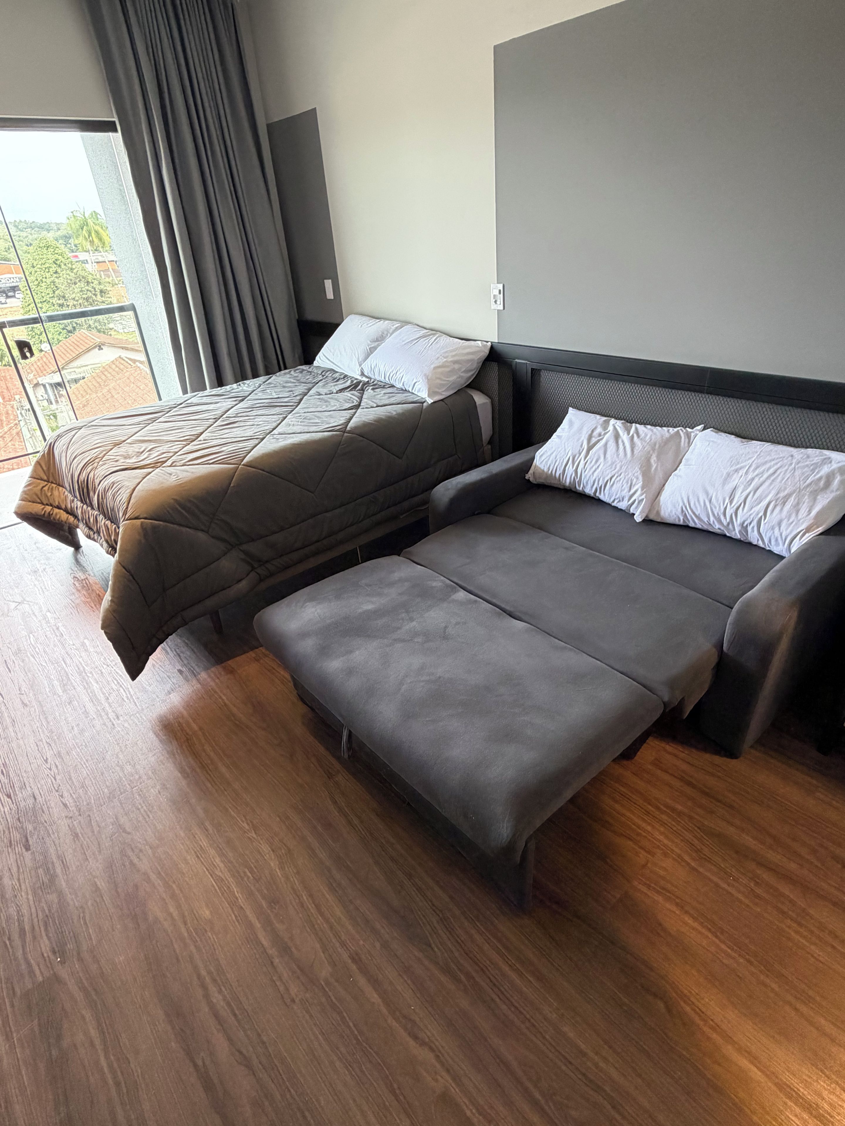 A modern bedroom with two beds, a sofa bed, and a balcony view.
