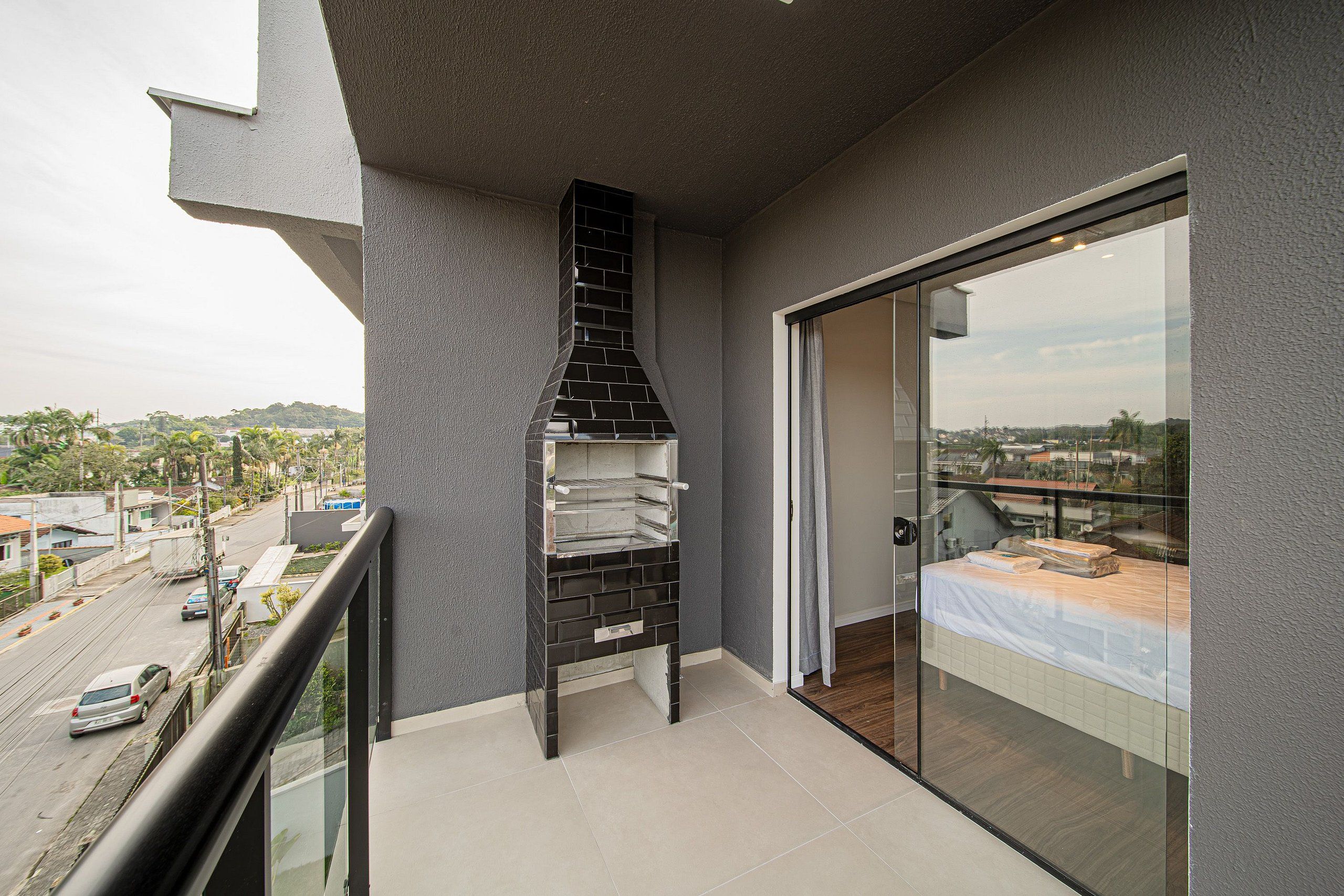 A balcony with a black grill, a glass door, and a view of the cityscape.