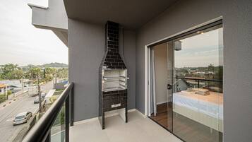 A balcony with a black grill, a glass door, and a view of the cityscape.