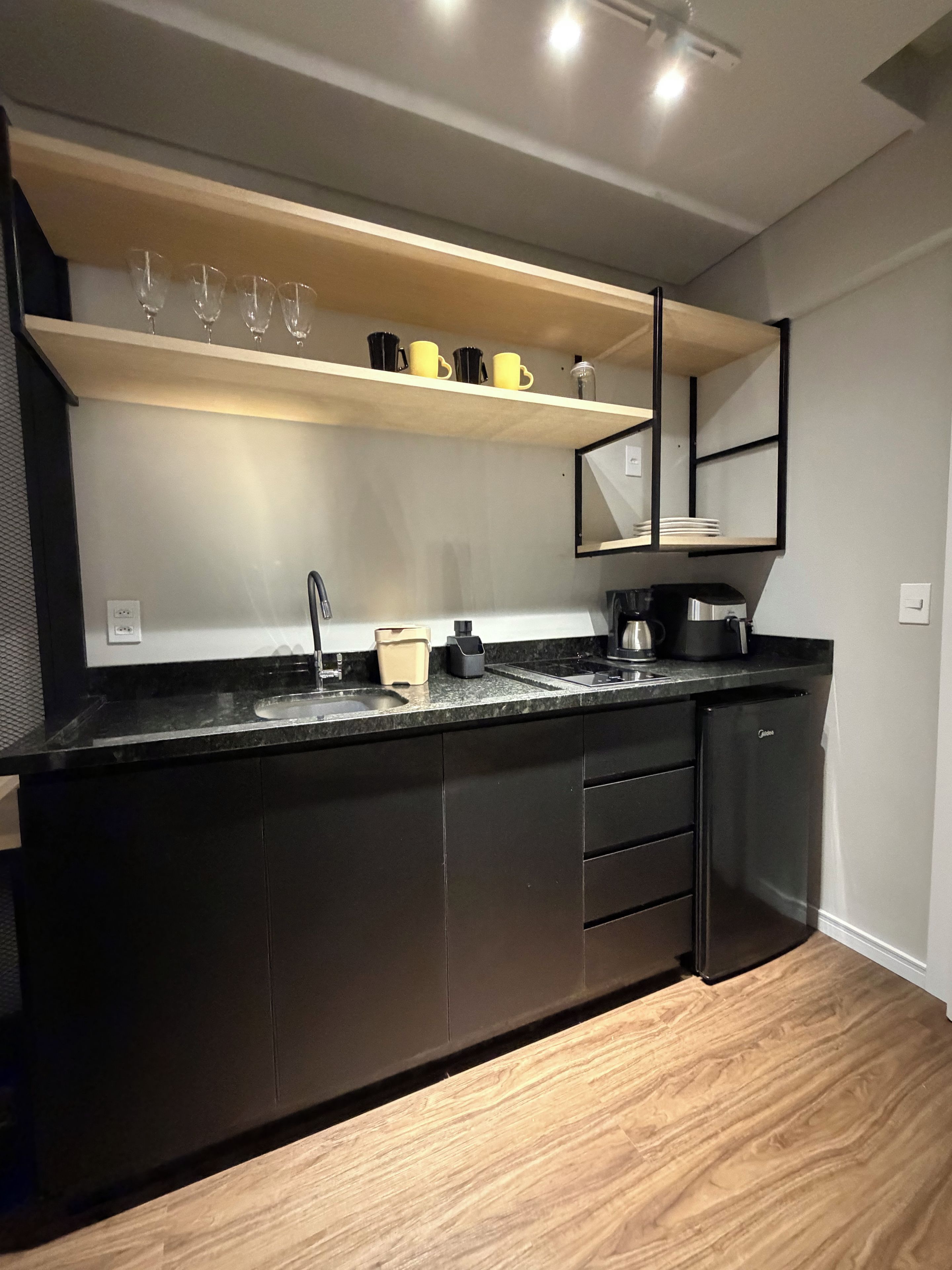 A modern kitchen with a black countertop, wooden shelves, and a built-in refrigerator.