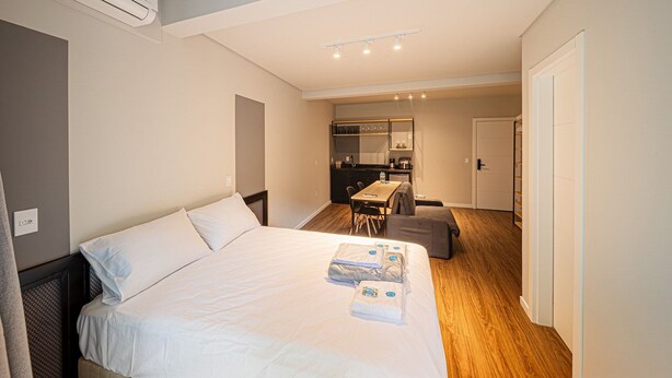Habitación de hotel con cama, kitchenette pequeña, mesa de comedor y zona de estar separada.