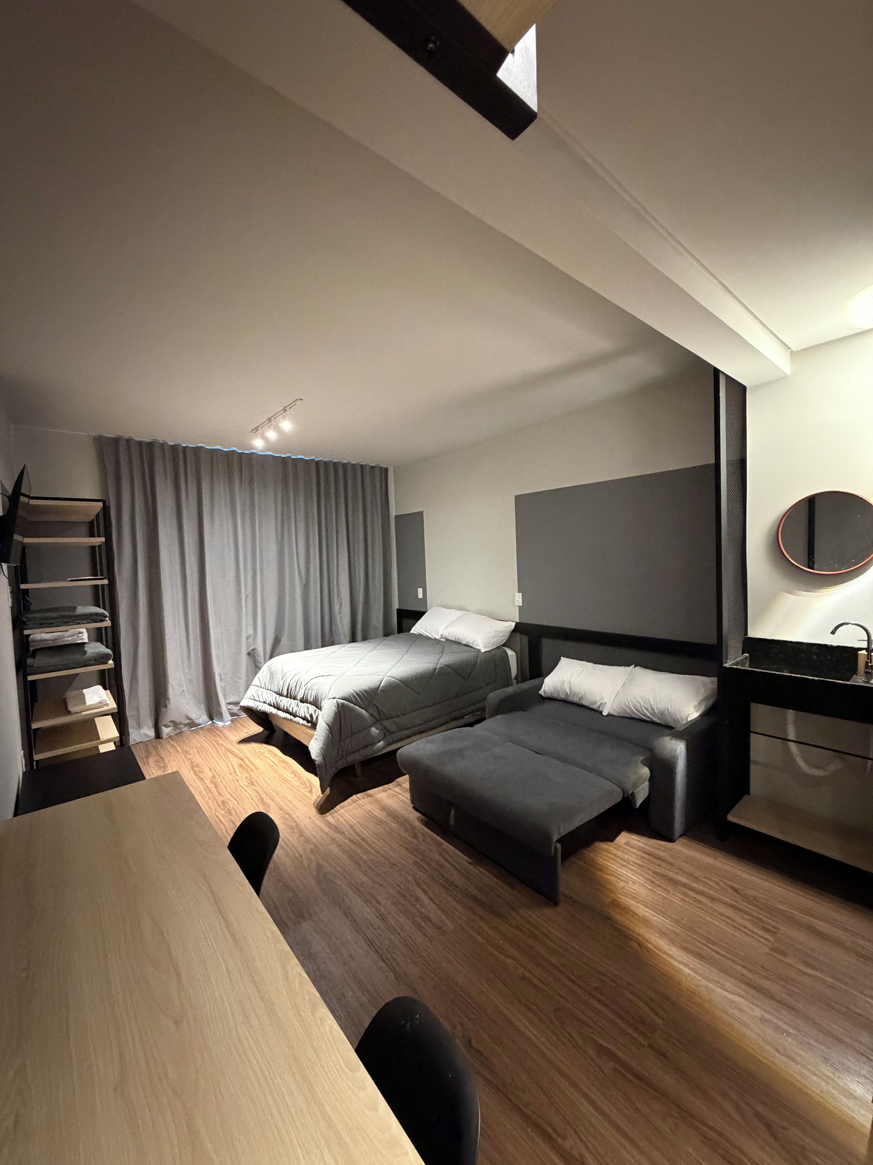 Quarto de hotel moderno com duas camas, uma escrivaninha, uma cadeira, uma mesinha, um espelho e um guarda-roupa.