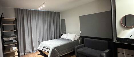 A modern hotel room with a bed, a desk, a chair, a wardrobe, and a large mirror.