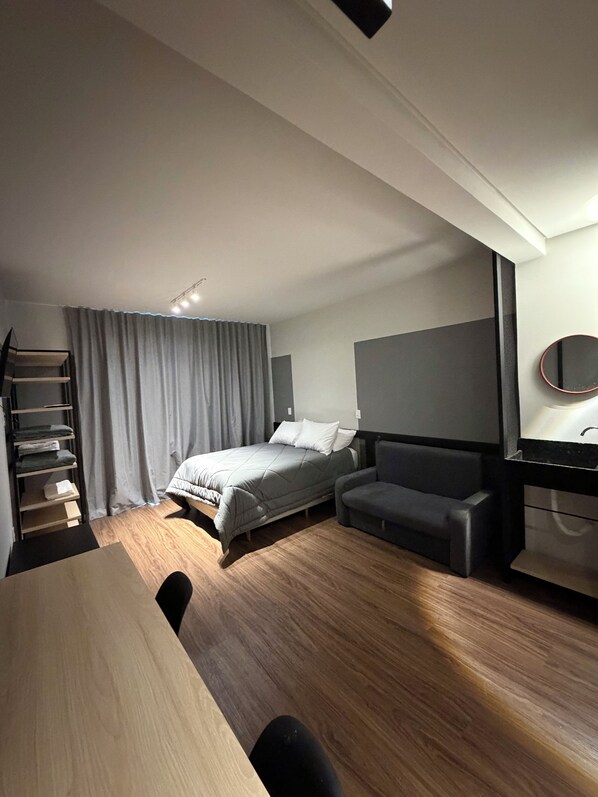 A modern hotel room with a bed, a desk, a chair, a wardrobe, and a large mirror.
