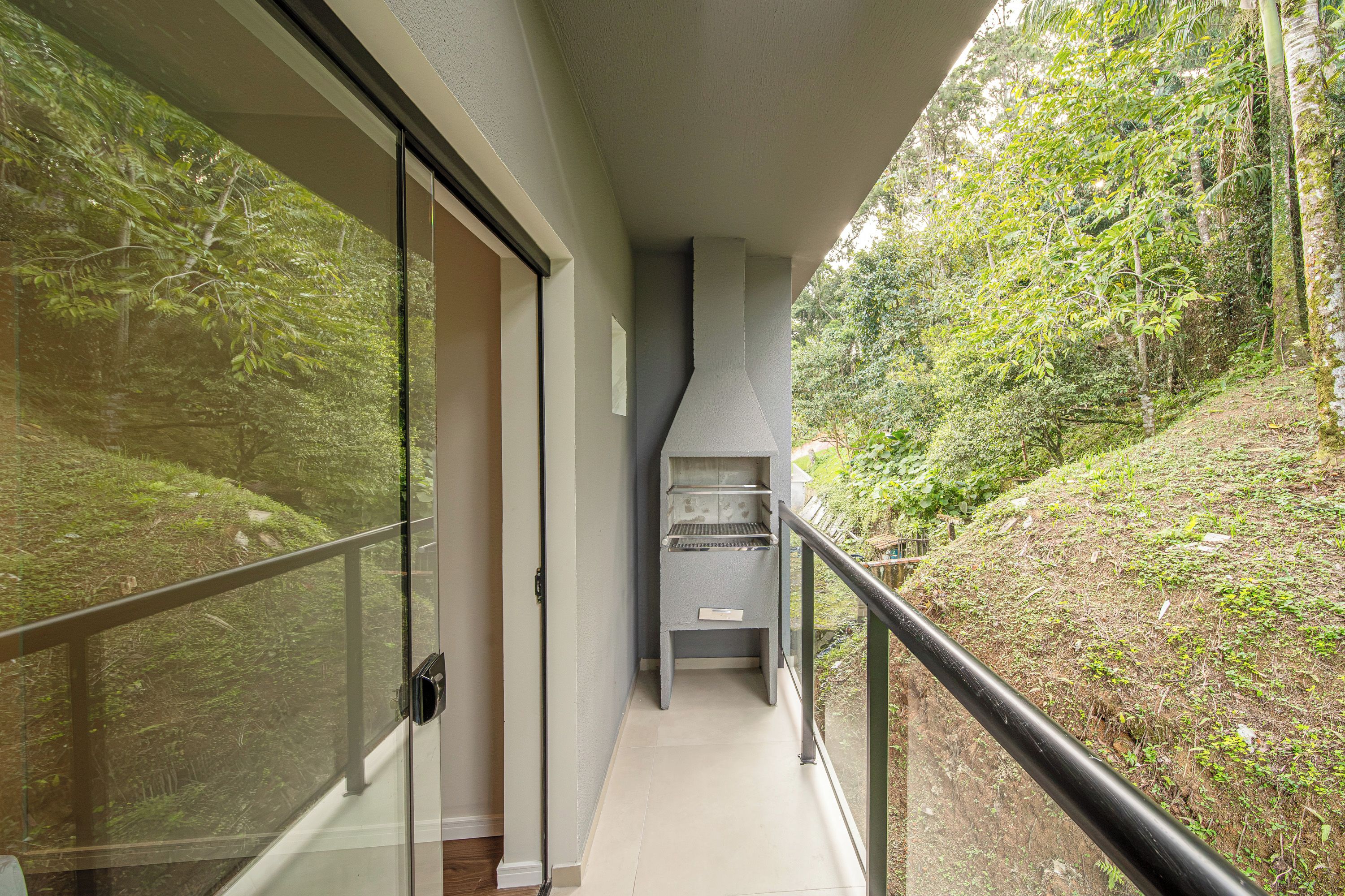 Un pasillo con una puerta de cristal que da a una habitación, una barandilla negra y vistas a una ladera boscosa.