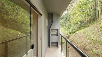 Un pasillo con una puerta de cristal que da a una habitación, una barandilla negra y vistas a una ladera boscosa.