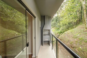 A corridor with a glass door leading to a room, a black railing, and a view of a forested hillside. - Apez Smart Studio (Joinville)