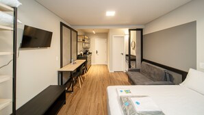 Una habitación de hotel con cama, escritorio, silla, televisión y baño.