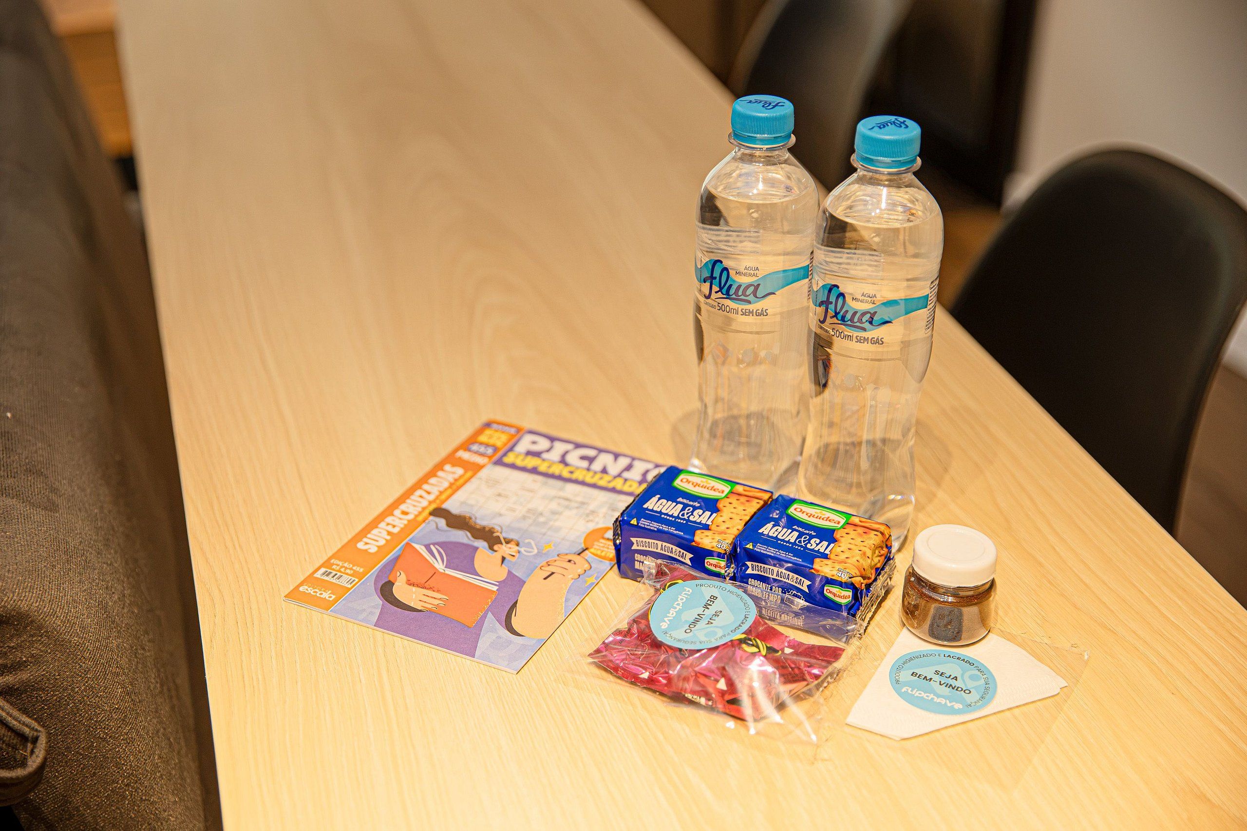 Una mesa de madera con dos botellas de agua, una revista, un paquete de comida y un frasco pequeño.