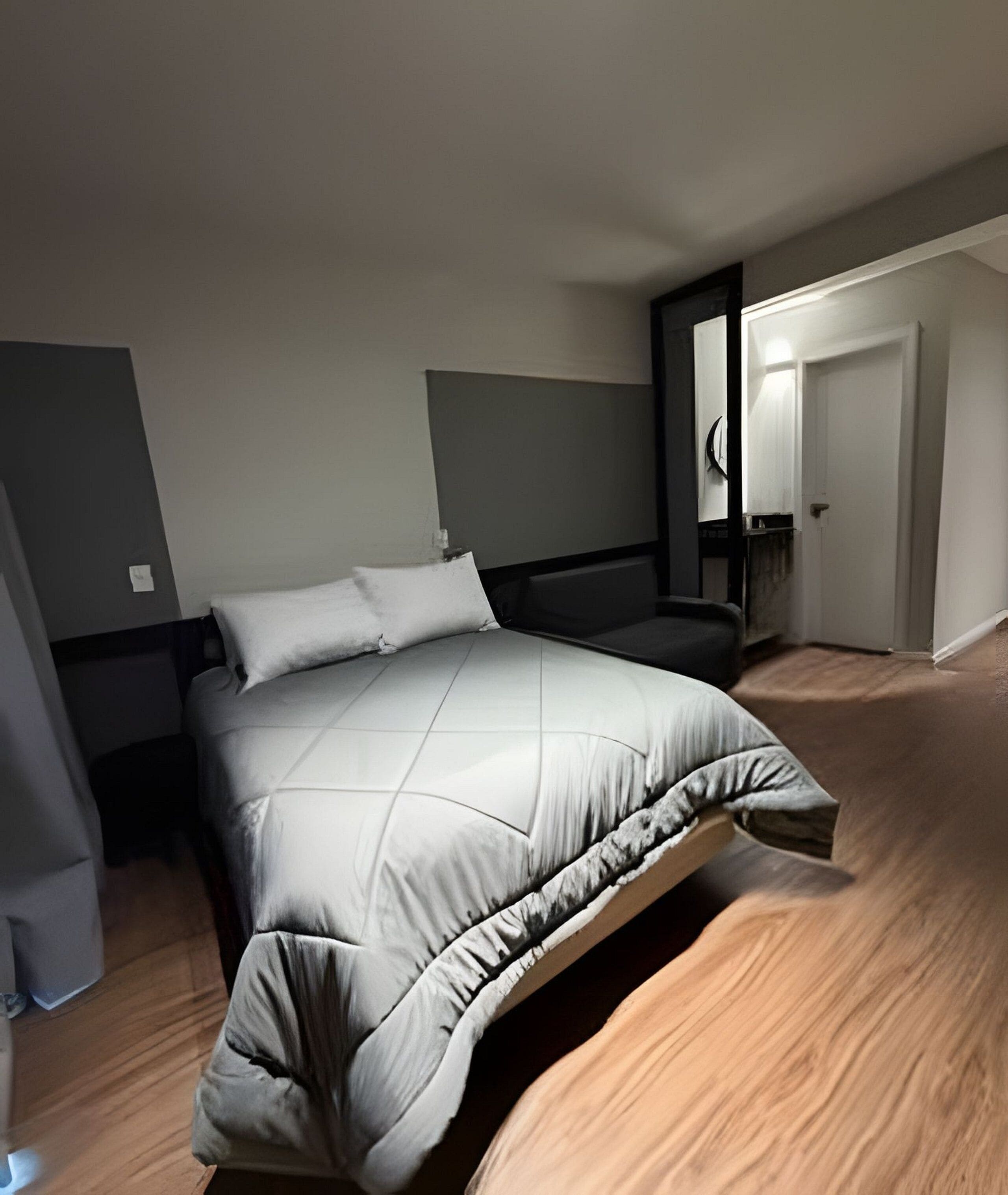 A modern bedroom with a bed, a nightstand, and a door leading to another room.