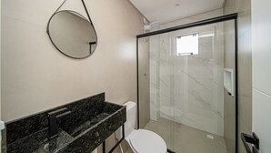 Un baño moderno con cabina de ducha de vidrio, un espejo redondo y encimera de mármol.