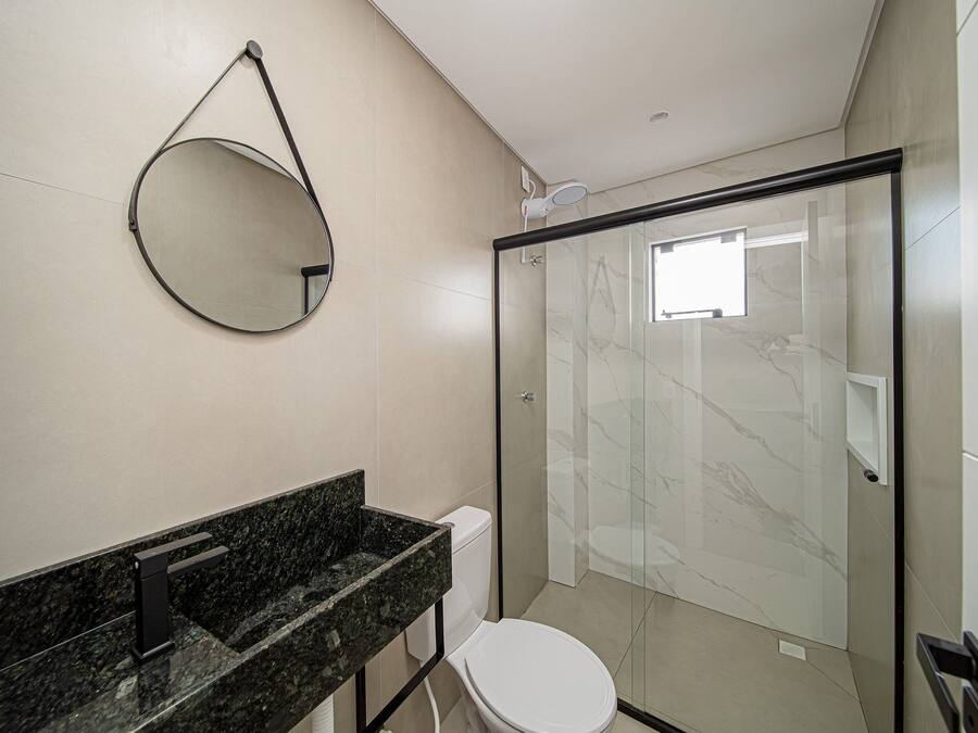 A modern bathroom with a glass shower enclosure, a round mirror, and a marble countertop.