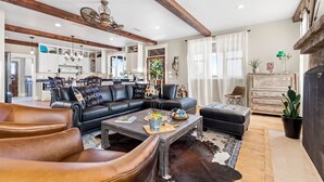 A spacious living room with a leather sofa, a coffee table, and a rustic fireplace. - TimberRose Ranch | Hot Tub + Hill Country Views (Fredericksburg)