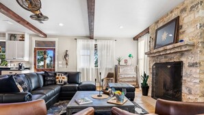 A living room with a fireplace, leather sofas, a coffee table, and a stone wall. - TimberRose Ranch | Hot Tub + Hill Country Views (Fredericksburg)