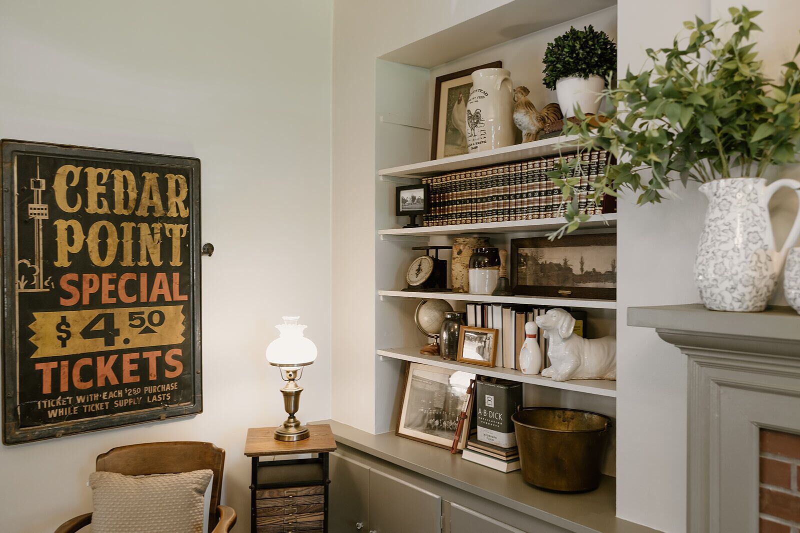 Ein Zimmer mit Schild für Sonderkarten für Cedar Point, einer Lampe, Regalen mit Büchern, Dekoration und einem Kamin.